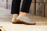 Person wearing Grey shoes with brown soles on a wooden floor.