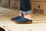 Person wearing blue slippers with 'glerups' branding on a wooden floor.