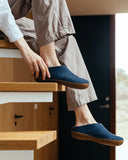 Person wearing blue slippers sitting on a wooden stool indoors.