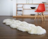 A fluffy off-white sheepskin rug laid out on a dark wood floor in a modern room setting with a red chair and wooden shelving in the background.